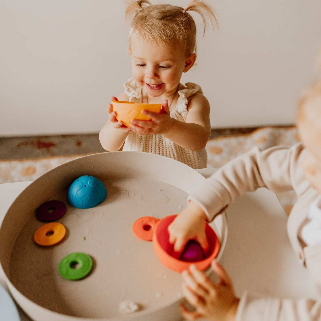 Toddler smiling playing with Ocean Stacking Cups in Bright and playing with the Tray Play and ice