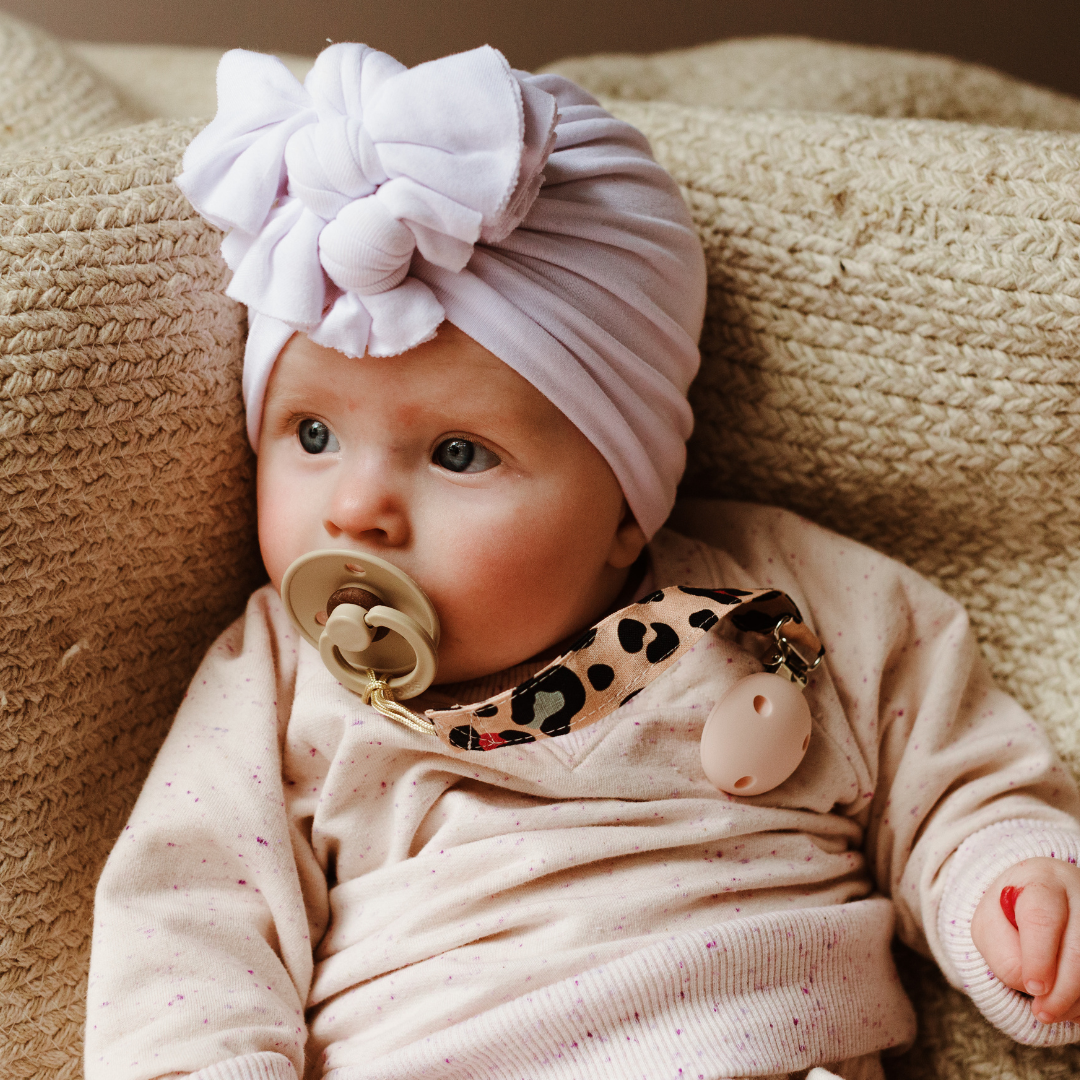 Baby girl with a dummy in her mouth on a dummy chain